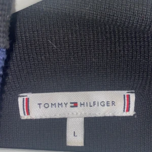 Tommy Hilfiger tröja, strl L - Högkrage, svart med marinblå glitter röd och vit rand på armarna. Litet märke längst ner. Väldigt skön och i bra skick. Säljs då den inte används.
