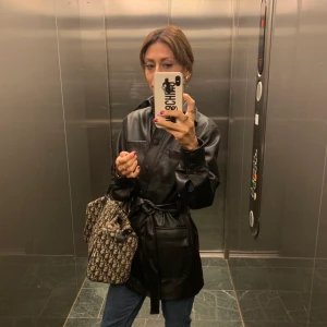 Jacka i läderimitation.  - Jacka i läderimitation med knytskärp i midjan från HM. Trendig 90tals jacka. Endst använd ett fåtal gånger. Ny pris 600-700kr (minns en exakt) 