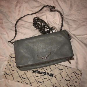 Zadig väska!  - Säljer nu min gråa Zadig Voltaire väska (äkta) i ”vanliga storleken” som jag köpte för 2 år sedan på Selfridges i London för över 3200! Den är inte i nyskick och har tappat lite färg (se andra bilden) på skinnet och silvermedaljerna, men inget som jag direkt tänker på 🥰 Dustbag + lång + kort kedja medföljer! Kedjorna är avtagbara och man kan välja vilket man vill ha! Fråga för fler bilder/frågor :) Bud: 950