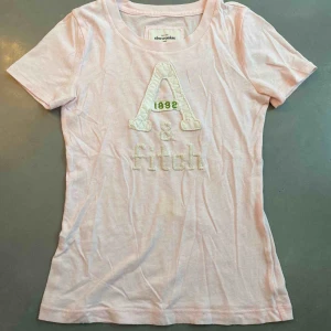  - T-shirt från Abercrombie and Fitch i storlek XS. Den har en liten gul fläck på magen men kan nog gå bort i tvätten.