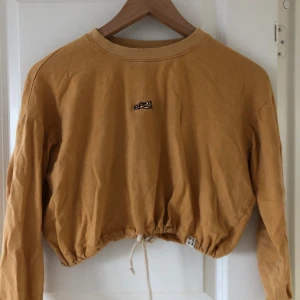 Kort hoddie från Bali - En cool kort hoddie som är köpt i en surfbutik på Bali, senapsgulfärg och vitt snöre som man kan dra åt i mitten. 