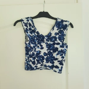  - Tight magtröja i vit med blått blommigt mönster. Kan passa en storlek S också men då är den inte lika åtsittande. Köparen står för frakt. OBS, katt i hemmet.
