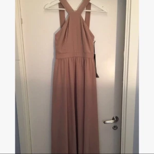  - Beige/ljusrosa balklänning. Nyskick och endast provad en gång, prislapp kvar! Väldigt bra kvalité och passar XS-S. Går ner till fötterna (för 165-170 cm). Sitter väldigt bra och har fin rygg!