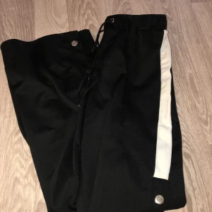 Utsvängda byxor  - Svarta utsvängda byxor med knäppningsdetalj längst benen som går att öppna för cool effekt. I bra skick! Strl S.