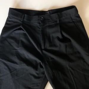Svarta kostymbyxor - Ett par svarta kostymbyxor i storleken 30(tum). Det passar som en XS-S. Den enda skadan är på knappen (bild 3) men det är inget som märks. Kan skicka close up vid intresse. Frakt 66kr