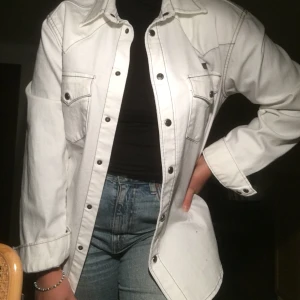Cool vit jeansskjorta  - Skjorta i jeansliknande material (jag har använt den som jacka), med tydliga sömmar i svart. Ett riktigt coolt plagg helt enkelt, som jag tror att någon annan skulle kunna använda mer än jag gjort. Superbra skick! Frakten ingår i priset