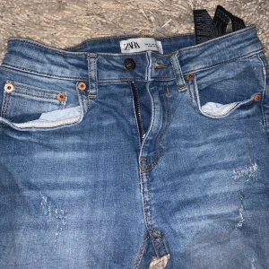 Blåa håliga jeans Zara - väldigt fina jeans från zara och är i väldigt bra skick, storlek Xs och är lite korta i modellen, Har slitningar på benen och längst ner men så var dom när jag köpte dom!