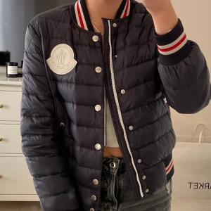 Moncler dunjacka - Världens snyggaste moncler jacka, i typ bomberjacka modell! Marinblå med vita o röda detaljer, självklart äkta! Storlek 12, men passar som xs (jag har xs/s vanligtvis)