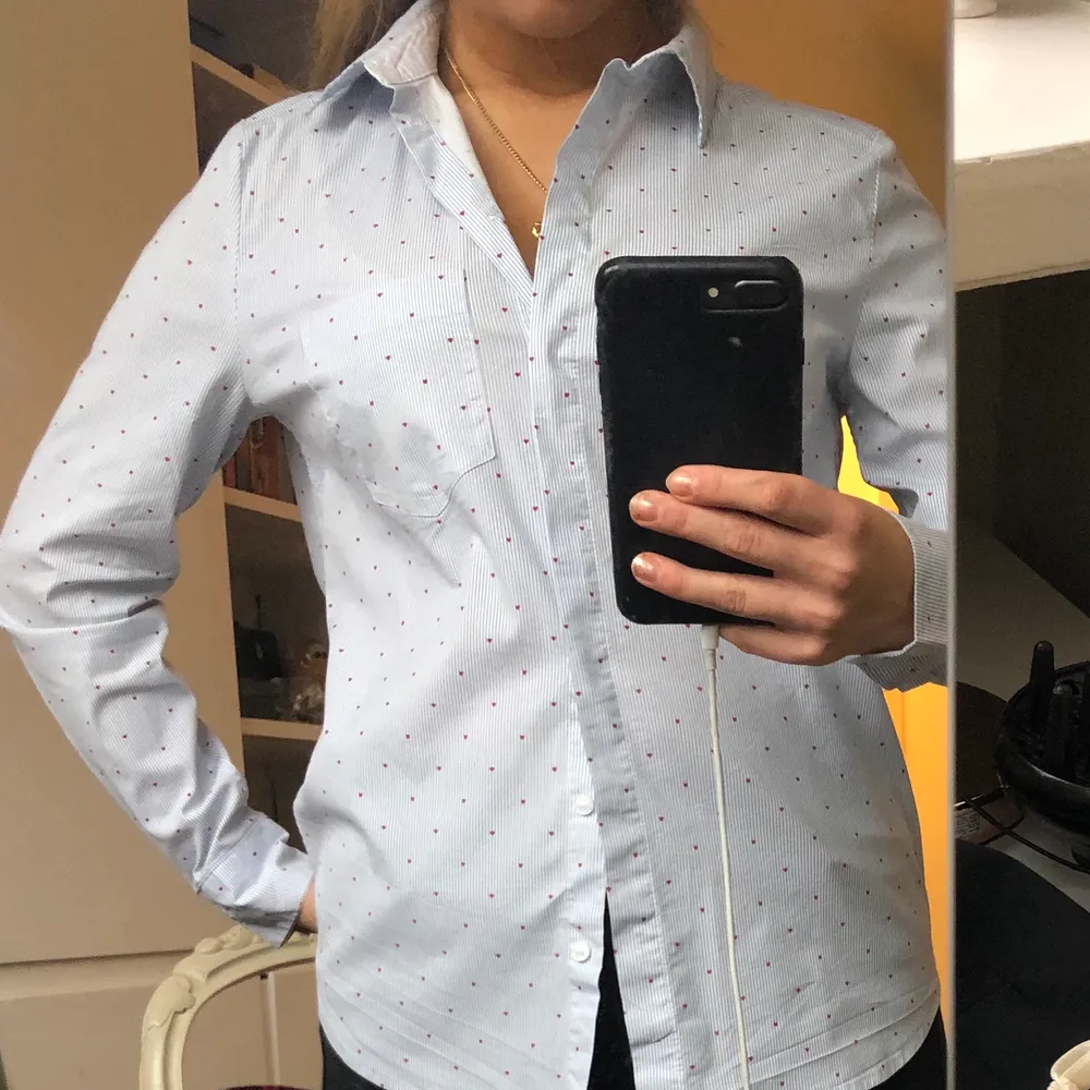 Jättesnygg skjorta från HM, som är tunt blå och vit randig, med små röda hjärtan på och en ficka över högra bröstet. Köpt för 200 kr säljer för 50 kr.. Skjortor.