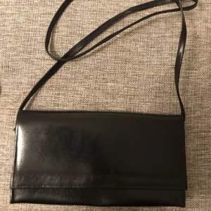  - Liten skinnväska (22x12cm) med axelrem, går att göra kortare om man knyter om, oanvänd. Vet ej vad det är för märke. Skickas endast, frakt ej medräknat i pris.