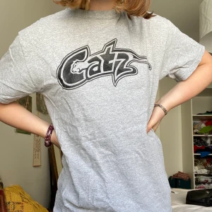 Grå Catz T-shirt  - Ljusgrå T-shirt storlek Xs-M beroende på önskad passform köpt på Beyond retro för 200kr. Frakt tillkommer