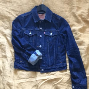 Levis jeansjacka XS - Mörkblå jeansjacka från Levis i storlek XS, stretch finns. Sparsamt använd. Tredje bilden visar innerficka som finns på båda sidorna. Armhåla till armhåla mäter 44 cm. Köparen betalar frakten och den skickas spårbart med postnord.
