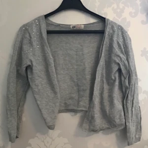 Kofta - Grå Kofta med diamanter påtill, tyvärr har det lossnat några diamanter som syns på bild 3 från H&M i storlek 134/140
