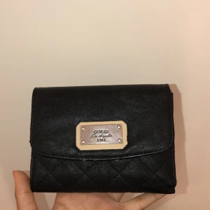 GUESS (äkta) - En jättefin Guess plånbok med mycket fina detaljer. Den har super mycket förvaring till både kort, mynt och även kontanter. Ordinarie pris: 600 kr