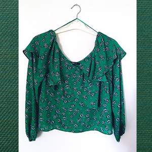 Grönblommig blus(artad) tröja från Gina Tricot i storlek 34, går ner över axlarna och ligger över barmen i volanger. Skirt och luftigt tyg (dock inte genomskinlig). Helt oanvänd med prislappen kvar!