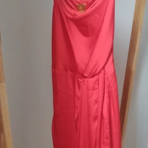 Klarröd silkig klänning - Helt oanvänd klänning i silkigt material med asymmetriskt axelband. Dragkedja i bak och justerbara axelband. Superfin men tyvärr för liten för mig. Kan postas, jag står för frakten.