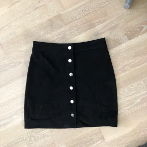 Mockakjol  - Är i storlek 36 men passar även en liten 38. Väldigt fin svart mockakjol med silvriga knappar längs framsidan. 