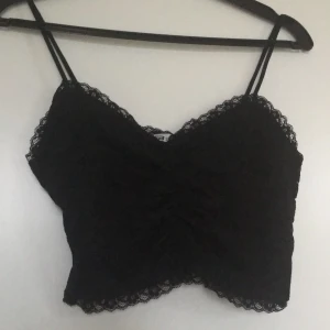 Svart crop top med spets stl s - Svart croptop som är rushad framtill och har dragkedja på sidan. 