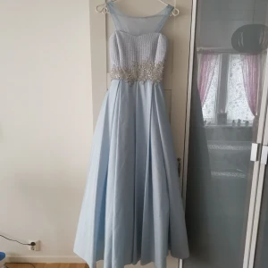  - Isblå festklänning  Använd endast 2 timmar (1 tillfälle) Nästan som ny! Mycket fint skick.  Storlek: 150-160cm Passar barn mellan 10-13 år (Töjbar bröst)  Kan fraktas! Köparen står för frakt! 