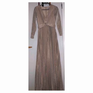Festklänning  - Sienna Lurex Gown Champagne  Har haft på mig den en gång. Storlek: 38 passar även 36 Ordinarie pris: 1199kr  - Stretchig kvalitet - Lätt omlott framtill - Avskuren i midjan med plisserad kjoldel - Slits framtill - Dold dragkedja i ryggen