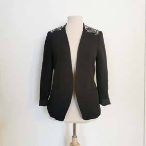  - Svart kavaj med pärlbrodyr. Märke: H&M. Storlek 36, lite stretching i materialet. Skick: Väldigt fint, använd ca 5 gånger. Pris: 150 kronor eller bud. Frakt: Betalas av köparen. 