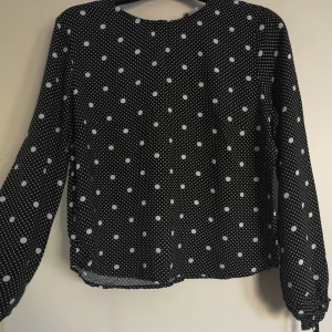 Svartvit prickig blus - Svart blus med vita prickar. Knappar längs med hela ryggen som går att öppna. Aldrig använd. Storlek 38 