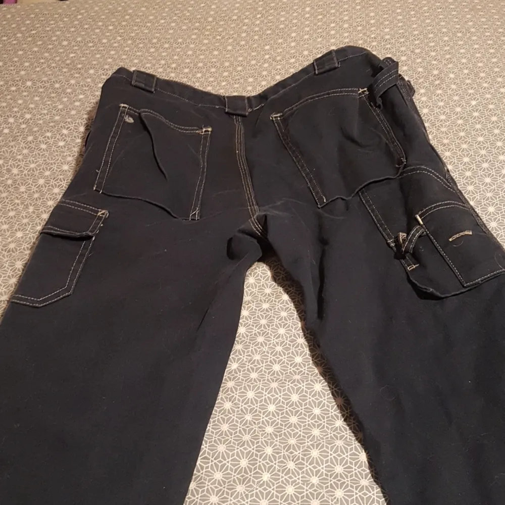 Det är ett par snickarbyxor med ganska många fickor dem är mörkblå och svarta, dem är gjorts i jeans.. Jeans & Byxor.