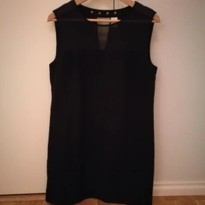  - Svart klänning från Vila. Transparant i övre delen fram och liten v-ringad öppning bak + små guldiga nitar. I begagnat men fint skick. 