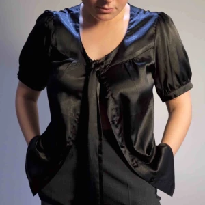  - Svart blus i glansigt material från Joy. Knyts framtill och går att knäppa. På bilden har vi den uppknäppt vilket också är snyggt! Storlek 42 men passar även storlek S eller M! 