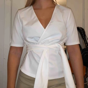  - Säljer en superfin vit blus från NA-KD, med stort brett band som man kan knyta hur man vill. Använd 1 gång, säljer pga att den är för stor för mig över bysten!💙