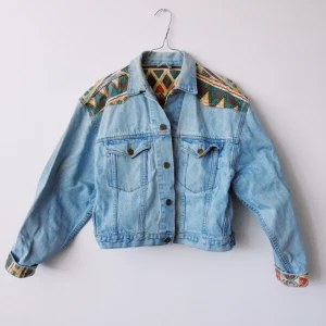  - Jeansjacka med fina detaljer av mönstrat tyg. Passformen är lite kort (men inte jättekort) och bred.  Kan skickas, mottagaren står för frakt.