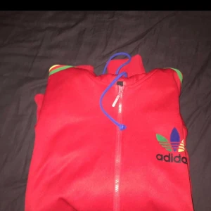  - Röd adidas hoddie med blå, gula och gröna sträck! I stort sätt helt ny! Storlek XL men passar L