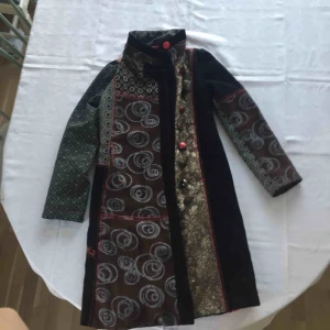  - Desigual ursnygg och unik lång jacka/kappa. Passar höst och vår. Mycket snygga detaljer, coola knappar, tyger och broderier. Bling i ögat på ryggen.