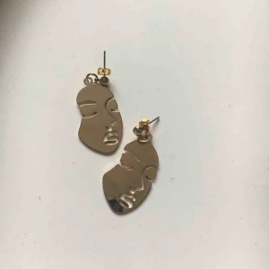  - Guldiga örhängen med ansiktsmotiv. Ej använda. Köparen står för frakten(9kr)