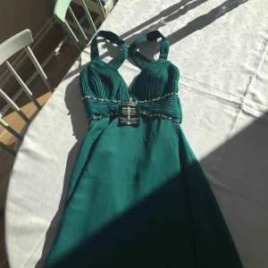  - Vacker långklänning i en smaragdgrön färg. Läcker lågskuren rygg och fina stenar. Något längre bak än fram. Oanvänd med lapparna kvar.