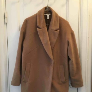  - Kamel-färgad kappa från Nelly. Storlek 36 men lite oversize och passar även 38. Dubbelknäppning fram och två fickor, passar lika bra till fest som till vardags.