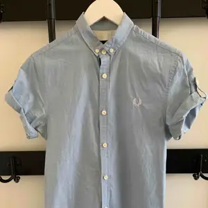 Slim fit short-sleeved dress shirt with cool details on the sides. Brand: Fred Perry Size: XS Fit: Slim Fit Colour: Light Blue  Used but still in good shape. really good fit. 