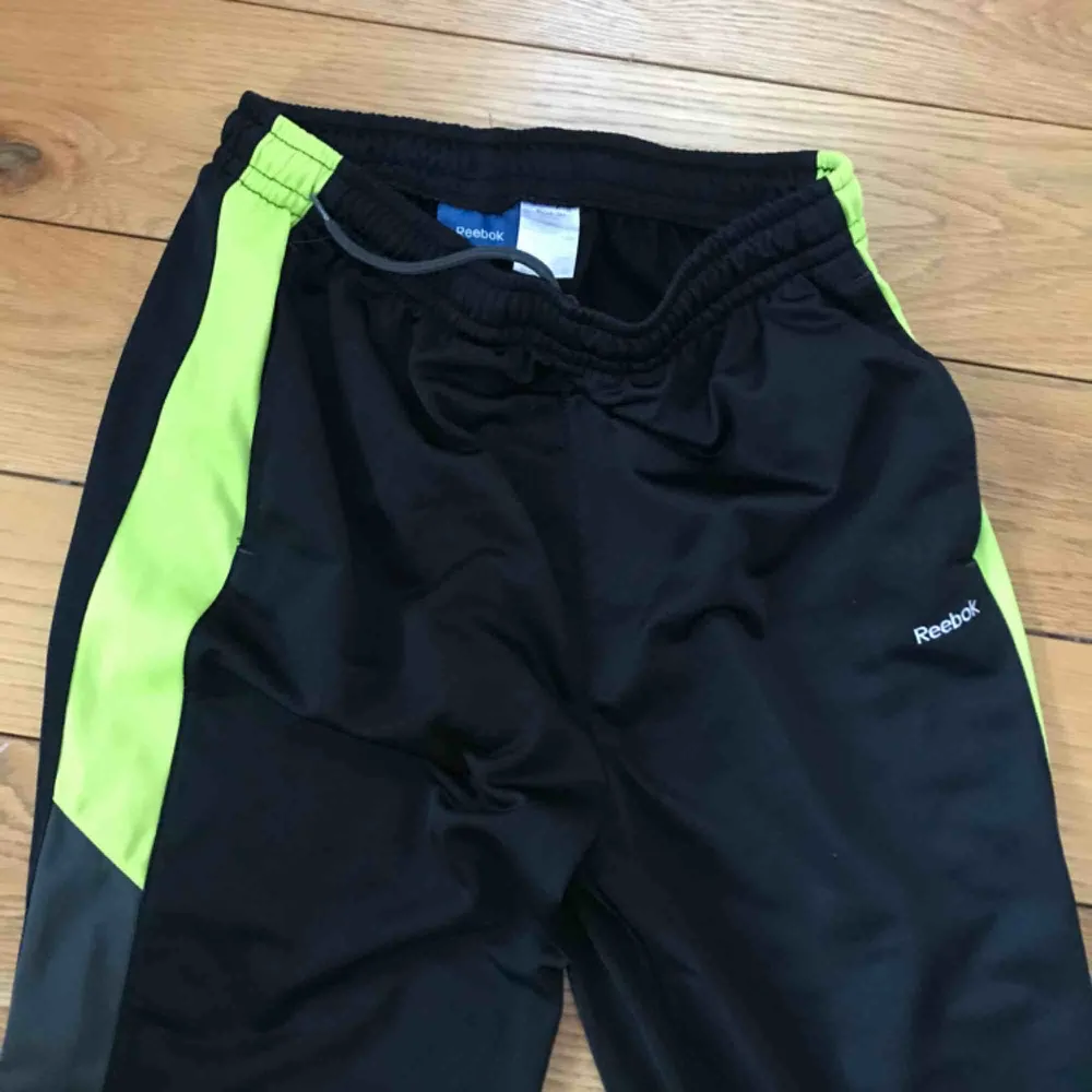 Snygga Trackpants i 90tals stil från Reebok. Svarta med lila och neongula detaljer. Perfekta till vintern! Avklippta nertill, längd cirka 30. Hög midja, så sköna och varma med mjukt foder. Köpta på Beyond Retro. Frakt tillkommer . Jeans & Byxor.