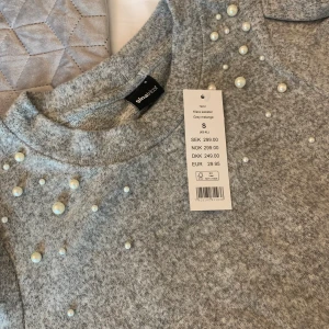 Stickad tröja - Grå stickad tröja med pärl-detaljer. Helt ny och oanvänd med lappen kvar. Den andra bilden är samma modell fast i svart för att visa bättre hur den ser ut på. 