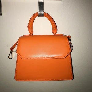 Orange, axelremsväska, nea bag, Gina tricot - Helt oanvänd, orange, axelremsväska från Ginatricot, storleken är 16*13, köpte den och en likadan rosa i somras för 280kr styck men har ej använt dom utan haft dom som dekoration hemma. Säljer en för 70kr och båda för 110kr, priset går att diskuteras. Deras riktiga namn är ”nea bag”. Det det medföljer även ett långt axelband så det går att bära dom både i handtaget och axelremmen.🧡🧡