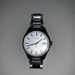 Calvin Klein klocka - Calvin Klein klocka som jag fått från en vän. Använd 1,5 år ungefär. Jag själv har aldrig använt den (herrmodell) men funkar nog för båda. Fin klocka med småsmå repor som inte syns. Har ej extra bitar man kan justera längden på armbandet. Batteriet är slut men kan bytas ut lätt. Spännet är viklås i stål. Är modellen K4M 211 och waterproof 3bar. Den är färg silver, rostfritt stål och safirglas. 40mm i diametern och armbandets bredd är 20mm. Nypris 1899kr mitt pris 600kr. Kunden står för frakten, kan också mötas.