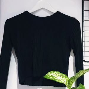 Ribbstickad svart tröja - Den hör tunna ribbstickade tröjan är perfekt för alla tillfällen. Klä upp med ett par större örhängen eller ett pampigt halsband eller ta på med ett par hög midjade jeans. Alla behöver en bra svart bas tröja med textur.