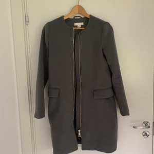 Grå Kappa H&M, strl 34 - Mycket sparsamt använd kappa med gulddetaljer. Mycket fint skick, storlek: 34. (Jag är 170 cm och den passar mig)