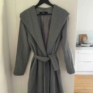  - Fin lång grå ullkappa. Stängs med knytbältet. 
