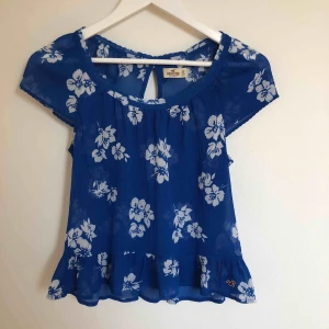  - Fin blå blus med vita blommor. Den är ganska transparent (se bild 2). Aldrig använd (pga att den inte passar mig).  Är i väldigt bra skick och bra kvalité. Frakt tillkommer.