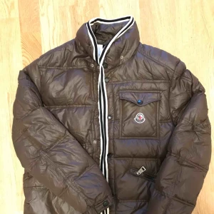  - Mörkbrun dunjacka från Moncler. Unisex, passar strl S-M, eventuellt L tack vare dubbelknäppning (bild 3: tjej med storlek S-M). Fint skick, väldigt varm.  Skickas mot fraktkostnad eller möts upp centralt i Stockholm/Huddinge senast 3/1-2019.