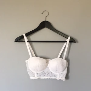  - Vit bustier med avtagbara axelband i fin spets. Silikon-linje på insidan av bh-n som går omkretsen runt för att förhindra att den åker ner när du inte har axelbanden. Bh-n är i nyskick och har fem hakar på baksidan av bh-n. Först till kvarn!
