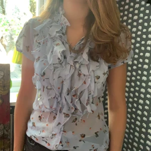 Ljusblå blus med detaljer  - En fin skjort tröja med blomdetaljer samt volanger där fram.