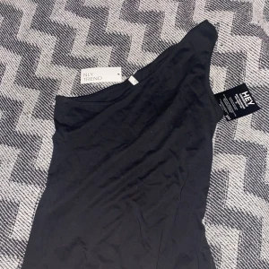 Svart one shoulder linne - Ej använt one shoulder linne med prislappen kvar. Stor i storleken så mer som S/M