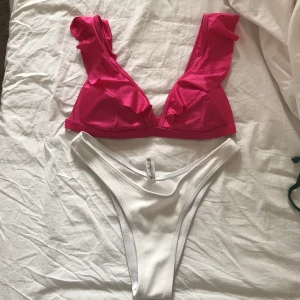 Bikini rosa + vit - Superfin bikini köpt på plick (aldrig använd av mig). Rosa topp med volang från Gina Tricot i storlek S. Vita bikinitrosor SÅLDA. Frakt tillkommer 💕
